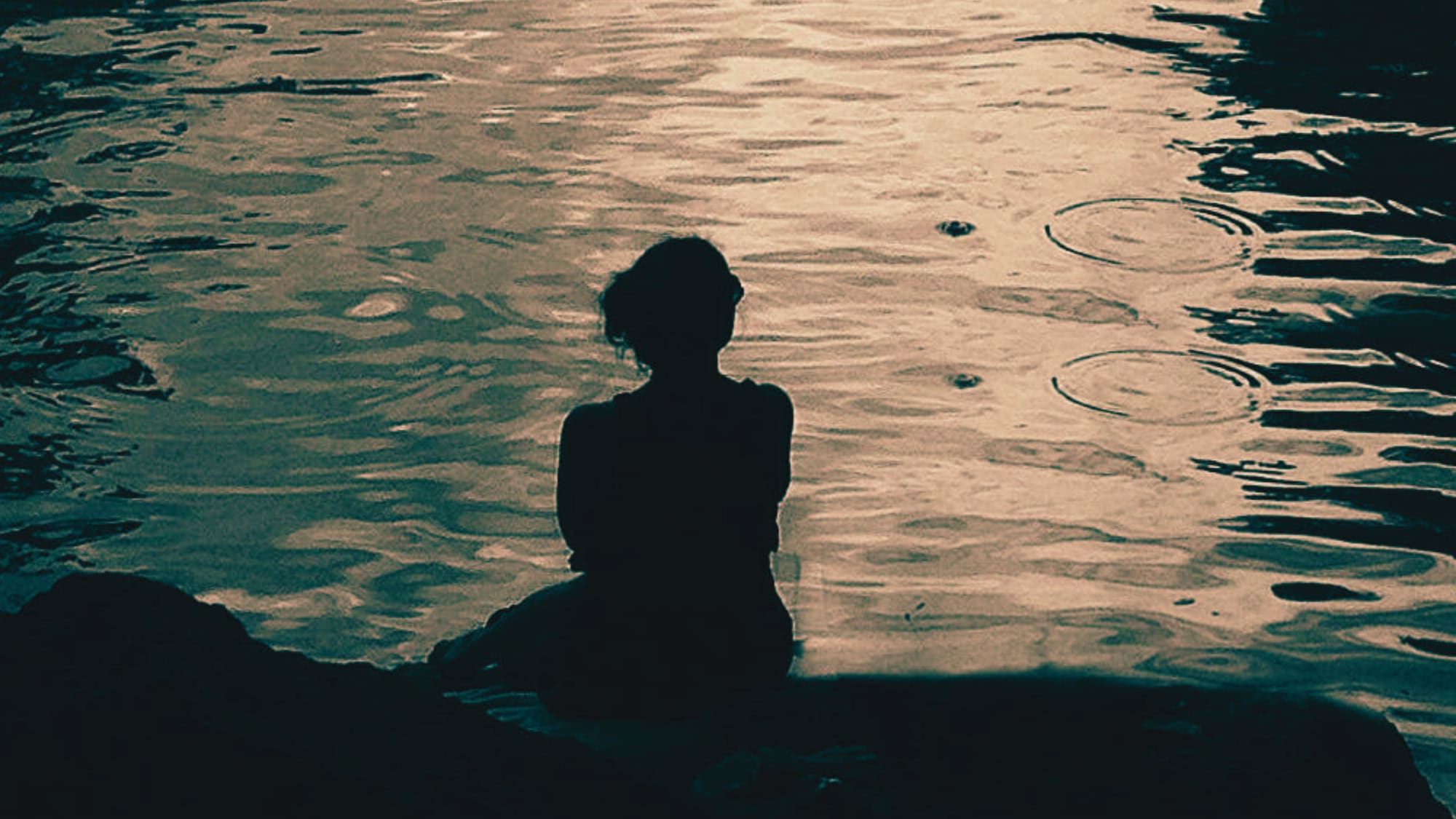 Silhouet van een vrouw in schemering aan het water